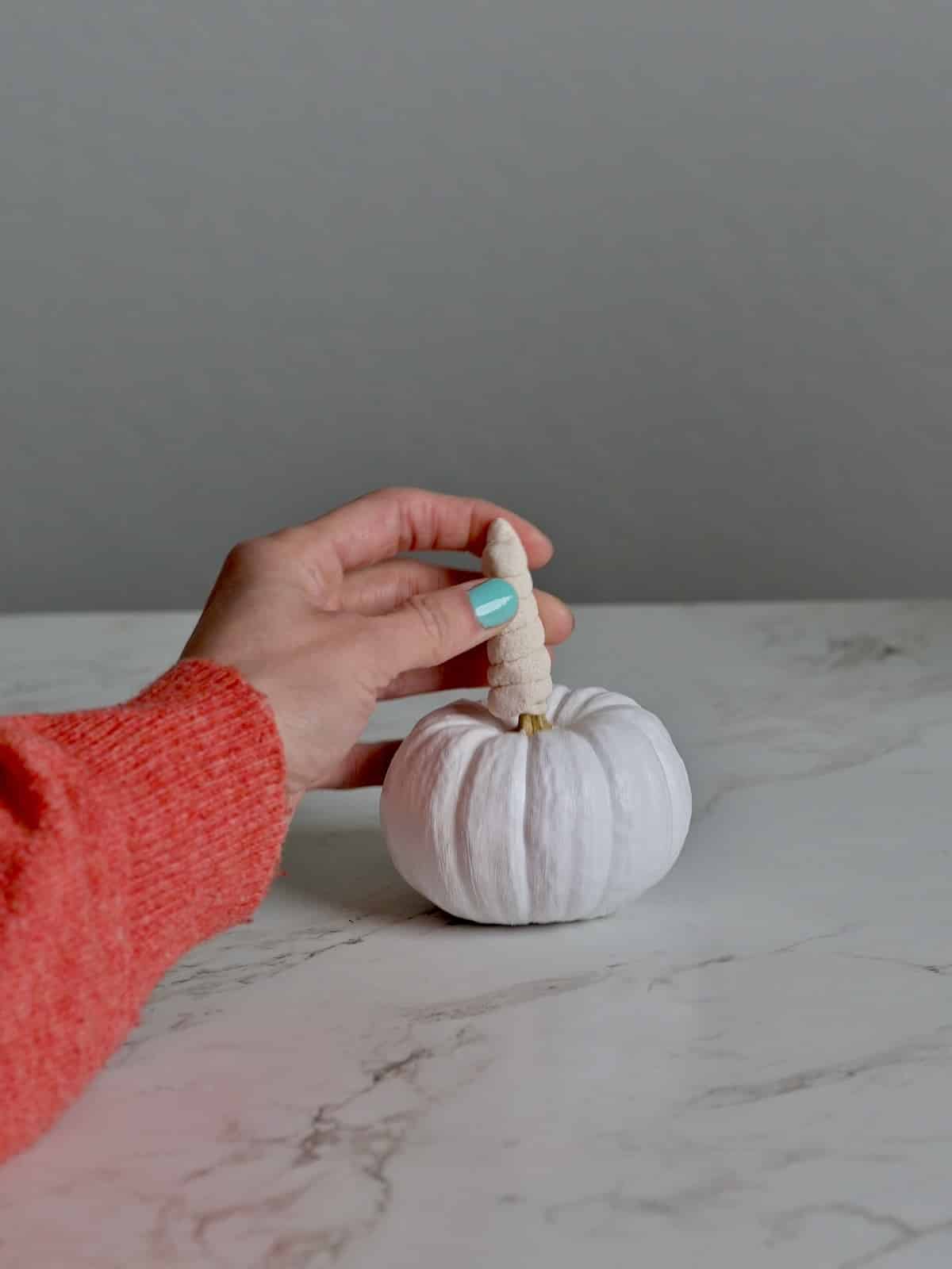 Air-dry clay shaped into a unicorn horn, being tested to fit on the unicorn pumpkin stem.