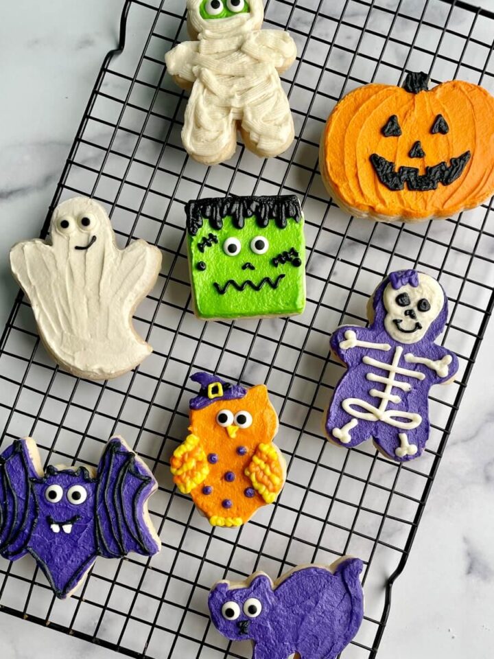 Several Halloween buttercream decorated sugar cookies on a cooling rack.