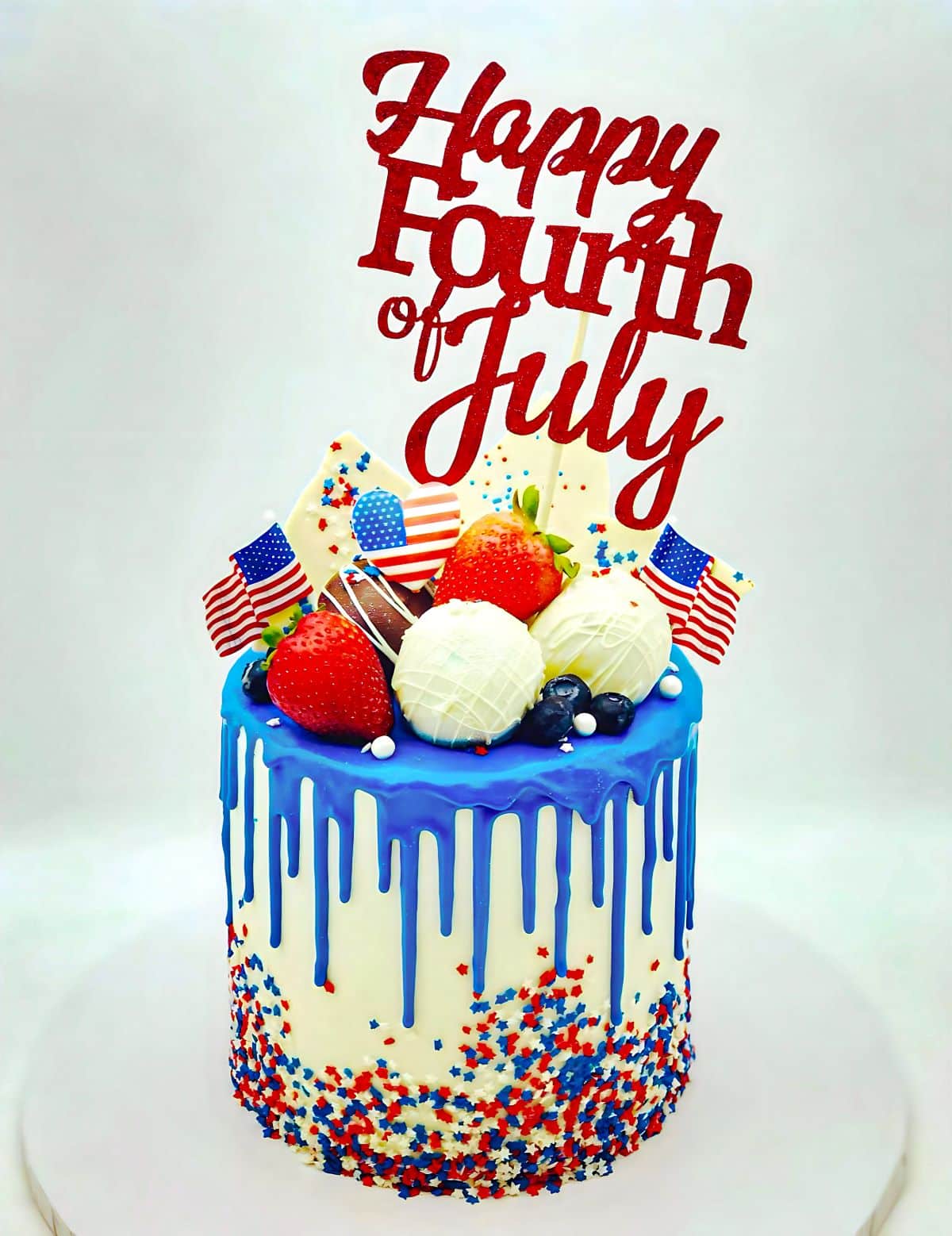 A cake banner that says "happy fourth of july" stuck into a tall decorated cake with red, white and blue.