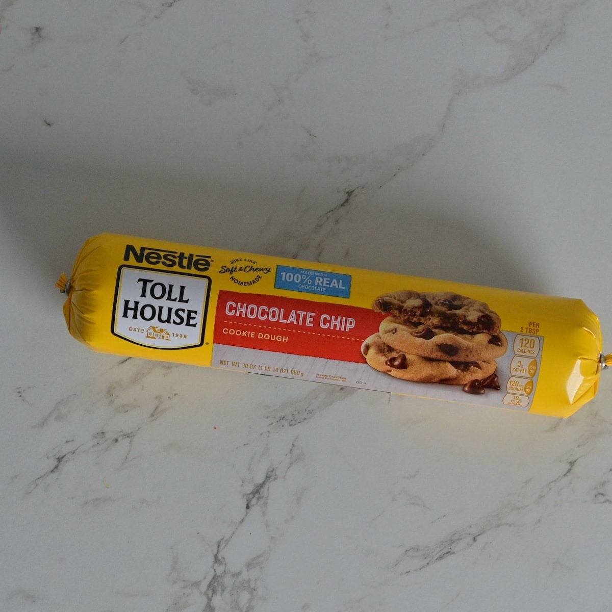 Roll of Nestlé Toll House chocolate chip cookie dough on a marble surface.